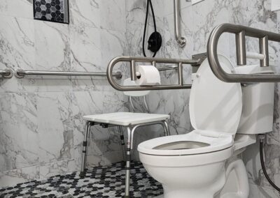 Accessible bathroom with white marble tile, a toilet with grab bars, a shower area with a seat, and black fixtures.