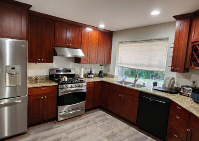 A modern kitchen featuring stainless steel appliances, granite countertops, dark wooden cabinets, and a window with blinds over the sink. The kitchen is well-lit and organized.